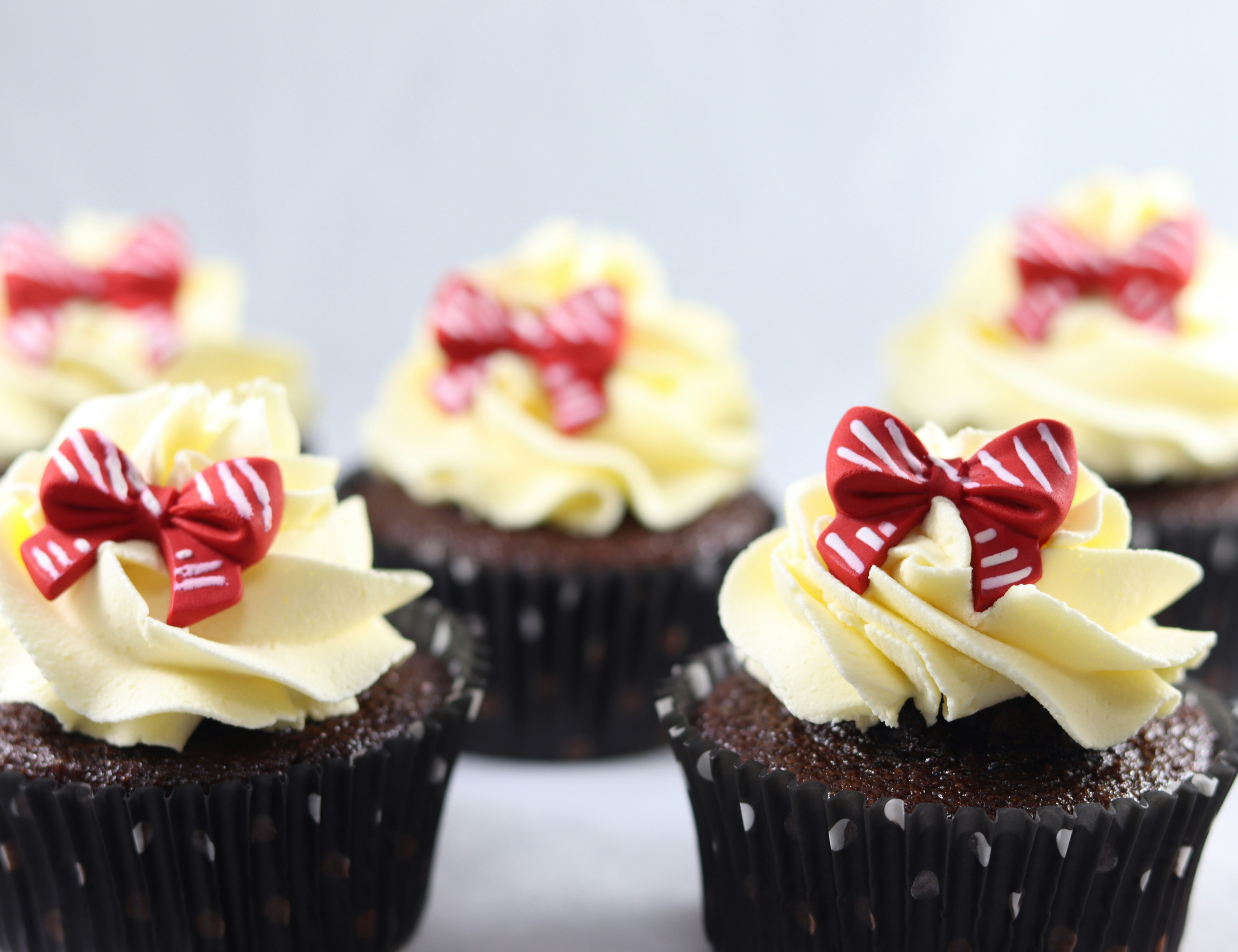 several chocolate cupcakes on a white background with yellow icing and red bows on top